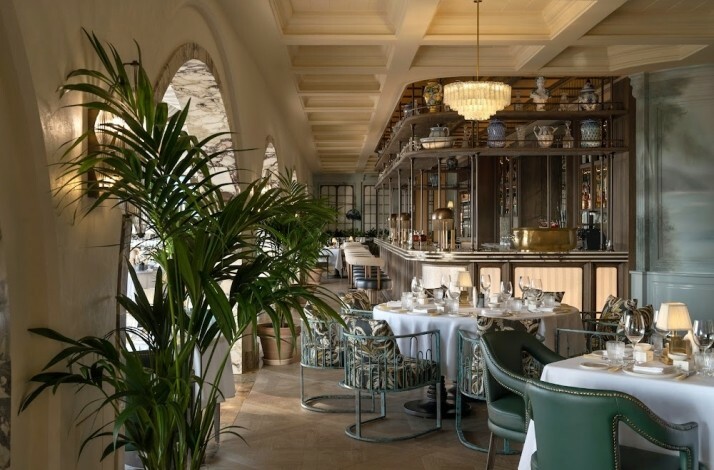Elegant dining room at Ristorante Loren with green velvet chairs, palm plants, and a marble bar.