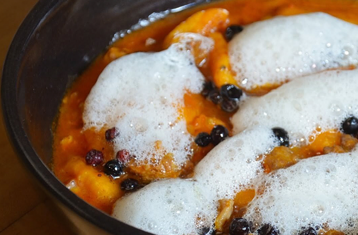 A vibrant dish featuring rich orange tones, light foam, and small berries that highlight the experience's innovative culinary approach.