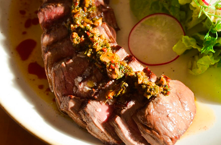 A juicy cut of meat served with a flavorful herb and spice topping, accompanied by fresh vegetables