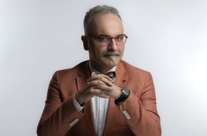 A close-up shot of historian Emrah Safa Gürkan posing with his hands clasped on the table.