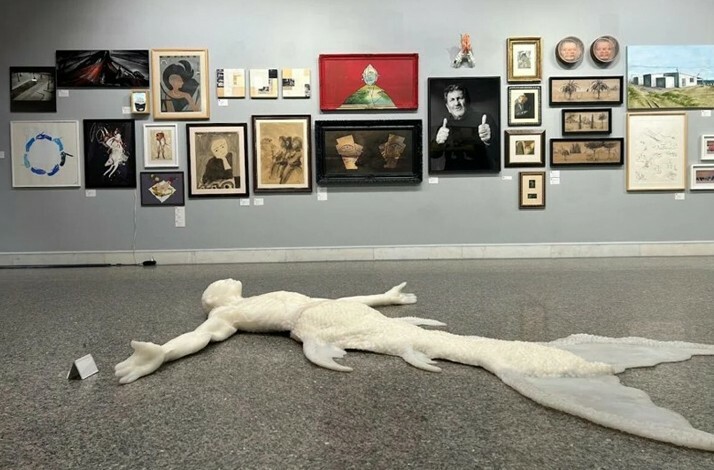 Image of many paintings from the Taviloğlu collection displayed on the wall and on the floor is an artwork that appears to depict a human and a mermaid together.