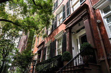 Tree-lined street in Greenwich Village, New York City, featuring classic red-brick rowhouses known as brownstones. 