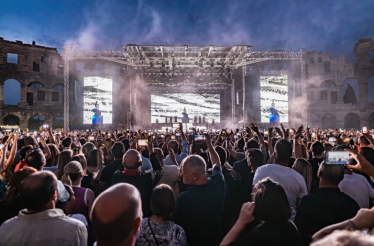 A large crowd watches a live concert at night inside the ancient Roman Pula Arena in Pula, Croatia.