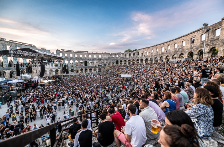 Packed concert crowd seated in the ancient stone tiers and standing on the floor of the Pula Arena in Pula, Croatia.