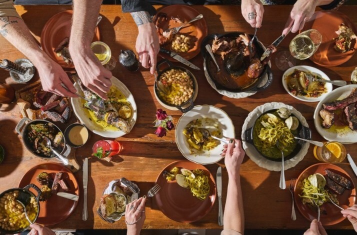 Diners sharing Italian dishes family-style at Peasant restaurant in NYC, rustic table filled with pasta, fish, and braised meats.