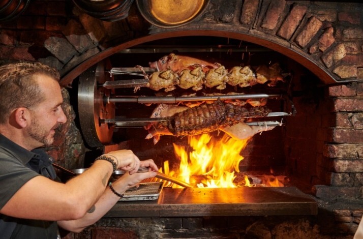 A chef grilling meat over open fire at restaurant Peasant.