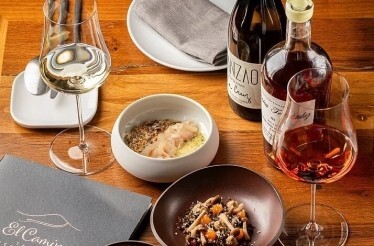 A gourmet meal with wine and artisanal dishes served on a wooden table at El Camino Tapas Restaurant.