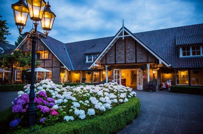 Exterior of Landhuishotel De Bloemenbeek in the Netherlands at dusk with glowing street lamps and blooming hydrangeas.