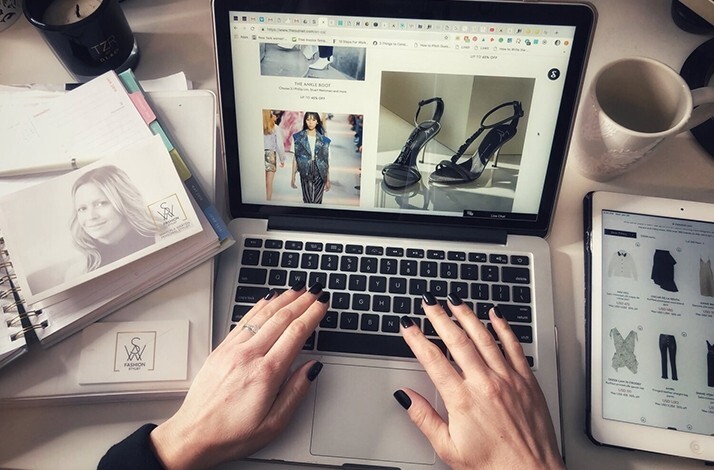 A pair of hands on a laptop crafting a moodboard with a black high heels and a black outfit on a model