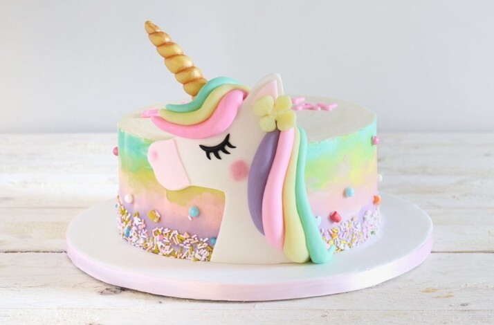 A cake coated with yellow, pink and green frosting with a unicorn icing decorated at the side