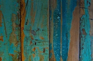 99 Restaurante - Close-up of weathered vertical wooden planks with worn turquoise paint peeling away to reveal the natural brown wood grain beneath.