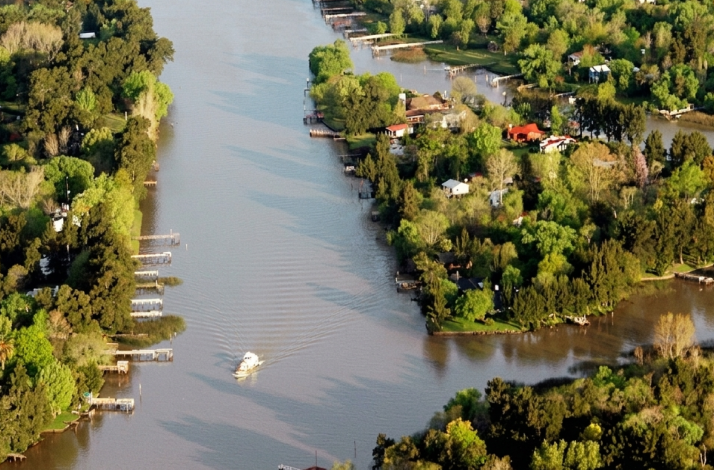 Aerial view of the Tigre River Delta, showing winding waterways, docks, and houses nestled among dense green trees.