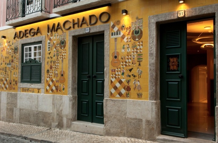 Yellow facade of Adega Machado in Lisbon, Portugal, featuring green doors and traditional music illustrations.