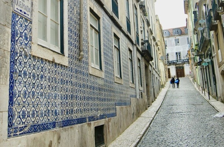 Historic cobblestone street in Lisbon's Bairro Alto lined with traditional blue-and-white azulejo tiles.