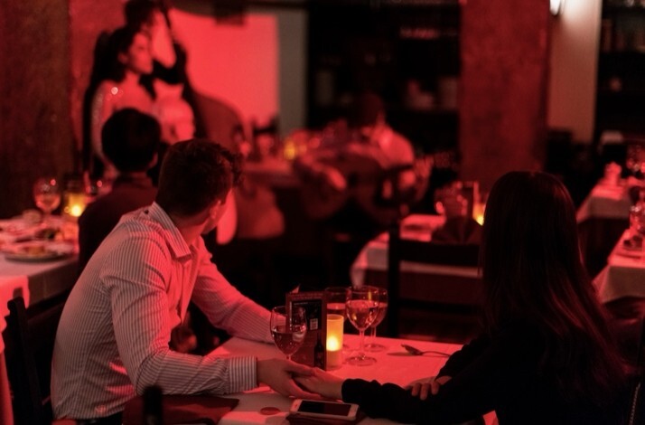 Diners seated at candlelit tables at Clube de Fado, Lisbon, with a guitarist performing in the background.