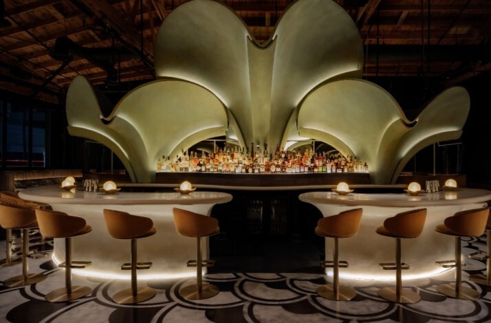 Grand curved bar at Lucia LA topped by an illuminated petal-shaped installation above a full spirits display.