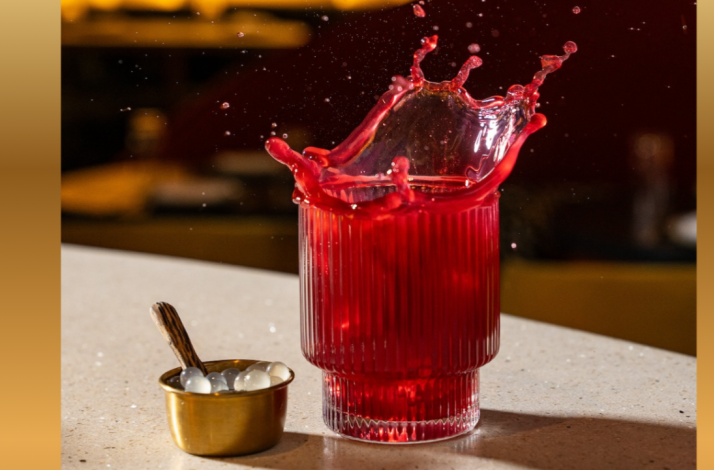 Deep-red cocktail splashing from a ribbed glass beside a gold cup of pearl garnishes at Lucia LA.