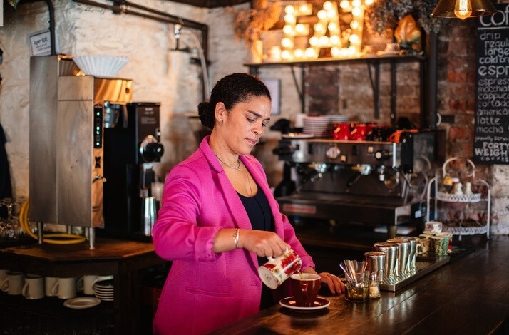 Co-owner of The Edge Harlem, Juliet in a pink blazer pouring drink into a cup at The Edge Harlem.