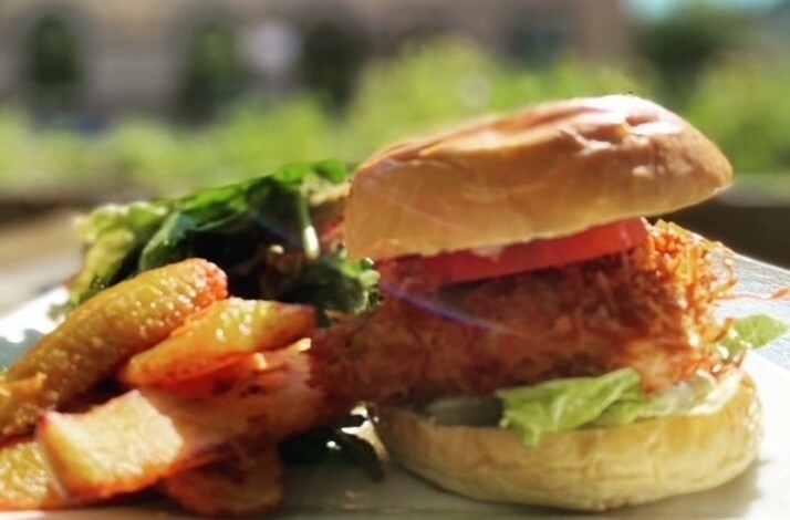 Crispy fried chicken sandwich with tomato and lettuce on a brioche bun, served alongside seasoned fries and a fresh green salad at The Edge Harlem.
