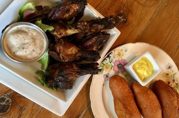 Smoky jerk chicken wings with dipping sauce plated beside golden fried dumplings and mustard on a wooden table at The Edge Harlem.