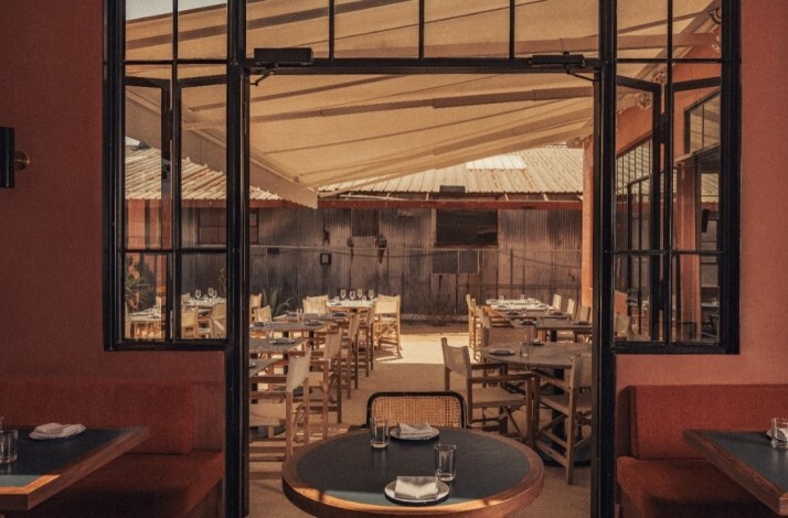 View from inside Loreto restaurant looking out to a shaded outdoor dining area with set tables and rustic decor.
