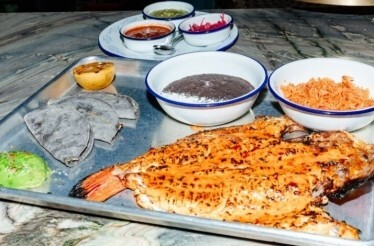 Grilled fish served on a metal tray with black beans, rice, blue corn tortillas, avocado, and assorted salsas in small bowls, served at Loreto.