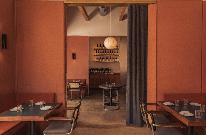Warmly lit interior of Restaurant Loreto with terracotta-colored walls, modern tables set for dining, and a view into a wine display area.