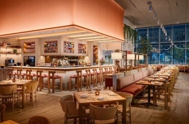Picala's warmly lit dining room at night, featuring a central bar, long banquettes, and floor-to-ceiling windows.