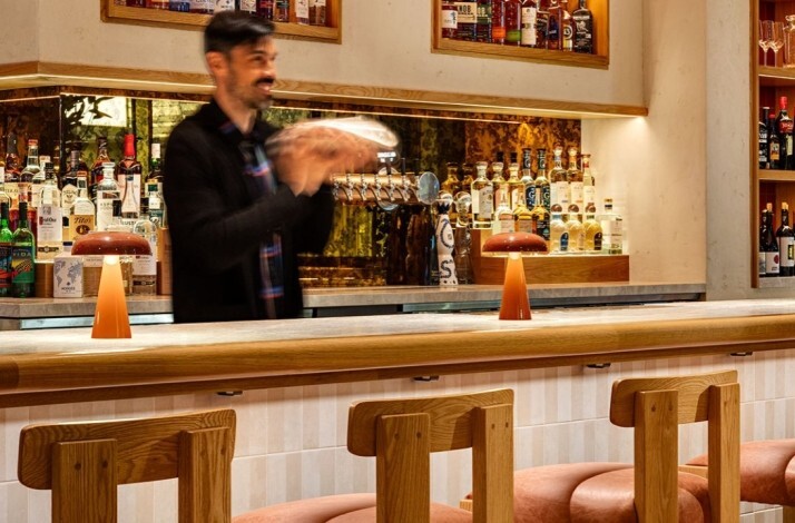 Bartender shaking cocktails behind Picala's warm wood bar, lined with spirits and amber mushroom lamps.
