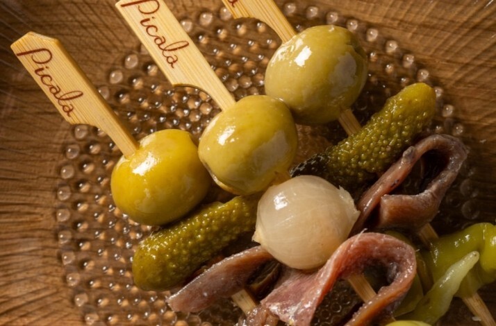 Picala's signature pintxos skewers with olives, gherkins, and anchovies, served in a dimpled glass dish.
