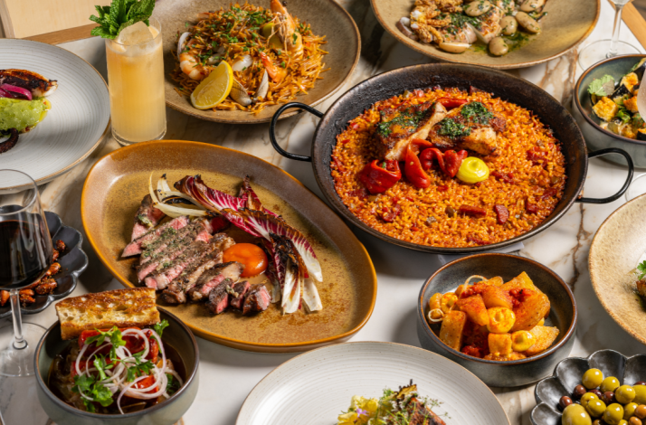 Picala's full table spread showcasing paella, grilled meats, olives, anchovies, and vibrant cocktails.