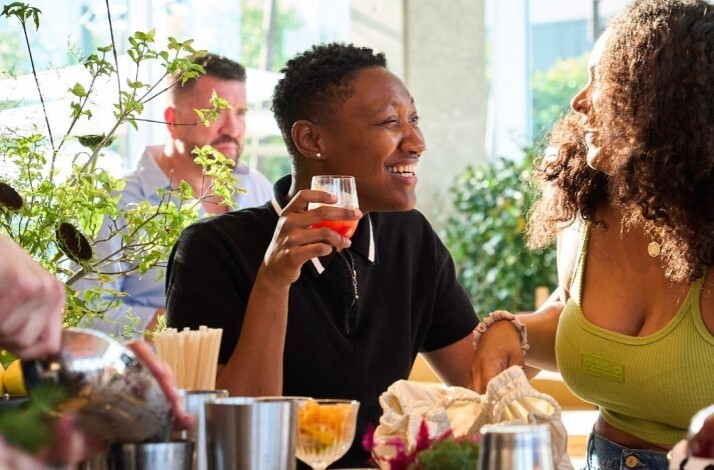 Guests socializing and holding cocktails at Picala's lively bar area, surrounded by fresh greenery and citrus.