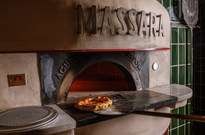 Massara's wood-fired oven with a freshly baked pizza resting on the stone hearth, framed by green tiles.