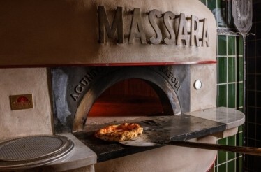 Massara's wood-fired oven with a freshly baked pizza resting on the stone hearth, framed by green tiles.