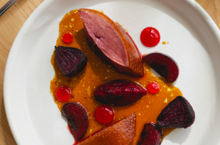 A dish of sliced duck breast, roasted beets, and glossy red sauce dots on a white plate served at Firstborn.