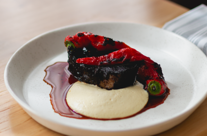A plate of charred red peppers and eggplant over a pale purée, surrounded by dark jus, served at Firstborn.