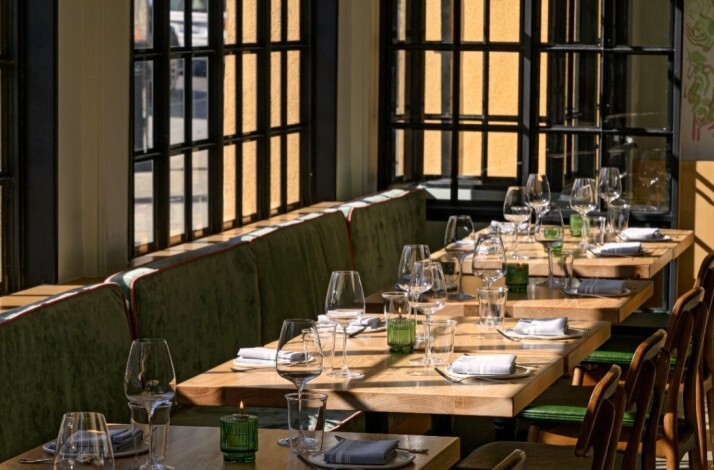 Dining area at Firstborn with sunlit window seating, set wooden tables, and a green banquette.