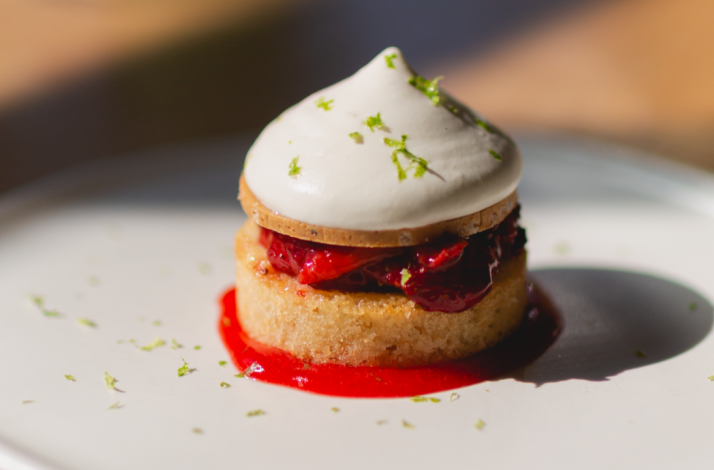 Dessert plate at Firstborn with a small layered cake, cherries, bright red sauce, and a dome of whipped cream.