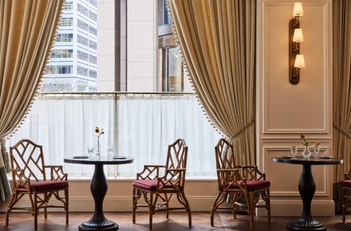 La Marchande dining area with bamboo-style chairs, round tables, and large windows with elegant gold drapes.