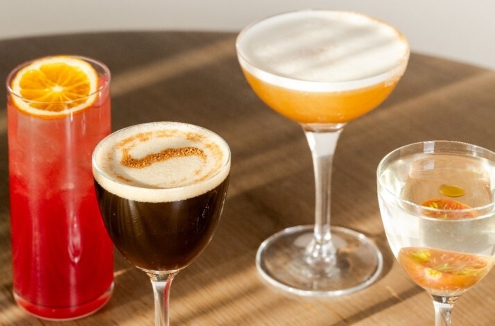 Assortment of handcrafted cocktails at North Fork Table & Inn, garnished with orange slice, edible flowers, and spiced foam, resting on a wood table.