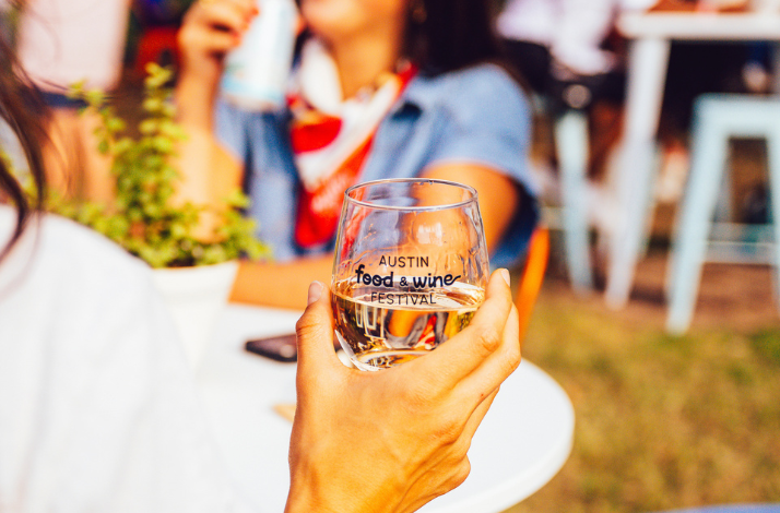 A guest holding a glass of water with the Austin Food and Wine Festival logo.