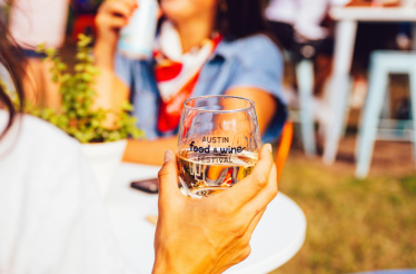 A guest holding a glass of water with the Austin Food and Wine Festival logo.