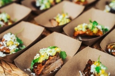 Rows of small cardboard trays holding grilled meat topped with corn salsa, crumbled cheese, and fresh herbs, served at Austin Food and Wine Festival.