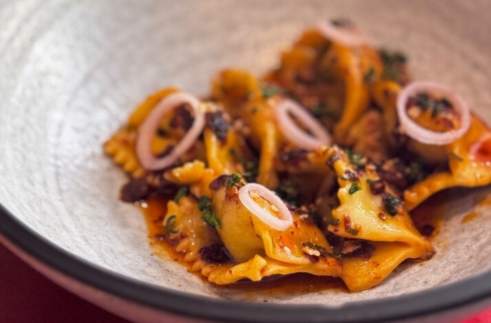 Braised dumplings in rich spiced broth, garnished with pickled shallot rings and fresh herbs, served at Zitz Sum.