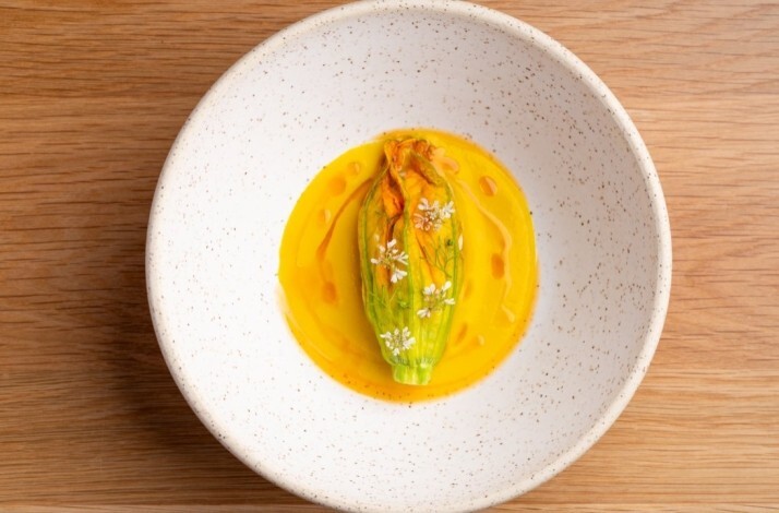 Stuffed zucchini blossom resting in vibrant golden sauce, garnished with tiny white flowers, served at Jacaranda.