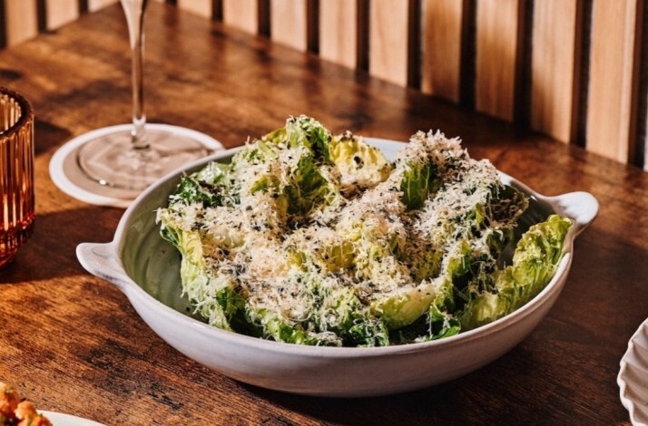 Crisp romaine salad mounded with shaved parmesan in a two-handled stoneware bowl on a warm wooden table at Little Water.