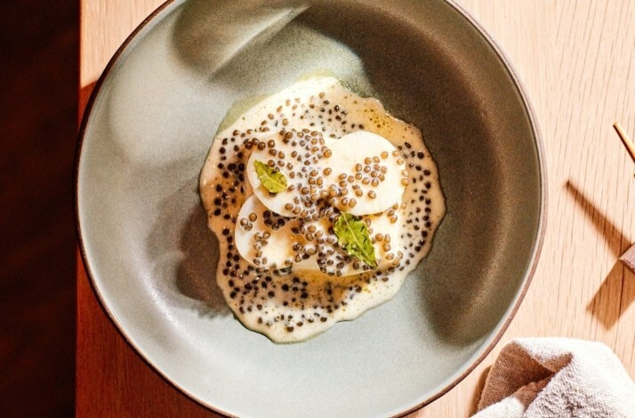 Overhead view of a small plated dish with creamy sauce and roe, with chopsticks resting on the table nearby.