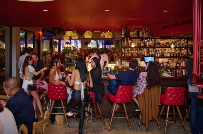 Lively bar scene at Michael's Genuine Food & Drink, with guests gathered around red-accented bar seating beneath warm pendant lights.