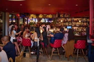 Lively bar scene at Michael's Genuine Food & Drink, with guests gathered around red-accented bar seating beneath warm pendant lights.