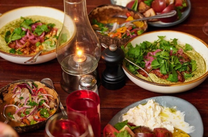 Multiple herb-garnished seasonal dishes sharing a candlelit wooden table at Michael's Genuine Food & Drink, Miami.